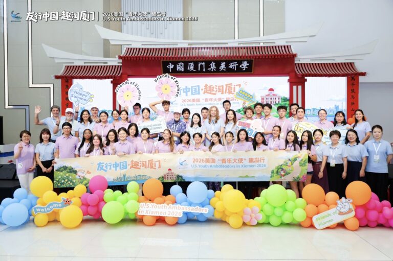 Opening of the Friends of Xiamen camp Large group of students in matching purple and lavender shirts in front of a stage with a Friends of Xiamen banner and balloons