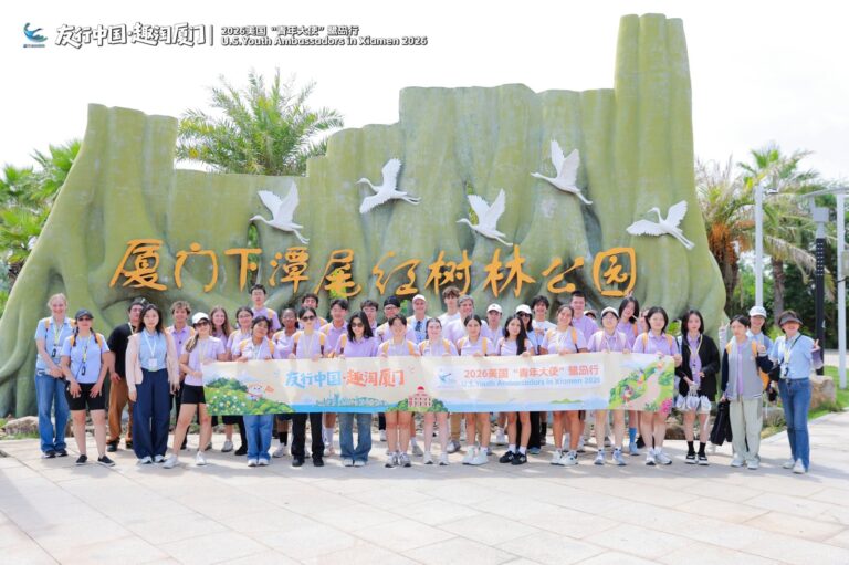 Xiatanwei Mangrove Wetland Park, Xiamen Group holding a banner in front of a green wall with the park name in Chinese characters and white bird sculptures