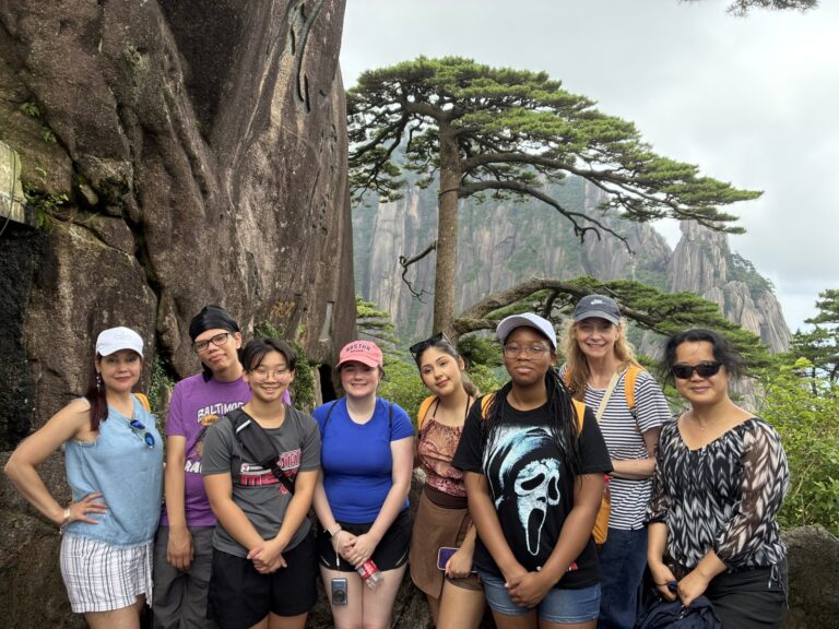 Huangshan, Anhui Province Ten people in hiking clothes in front of a pine tree with granite peaks behind them