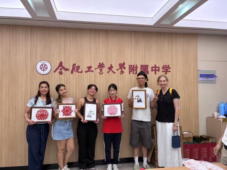 Student exchange at the Hefei University of Technology affiliated school Six students holding framed paper-cut artworks in front of a school sign