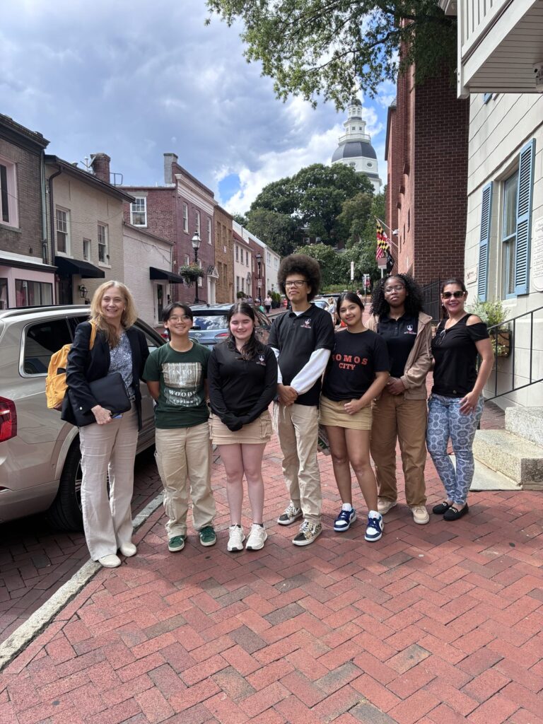 The Youth Ambassadors in Annapolis, with the State House dome behind them Five students and two adults standing on a brick street in Annapolis with the State House dome behind them